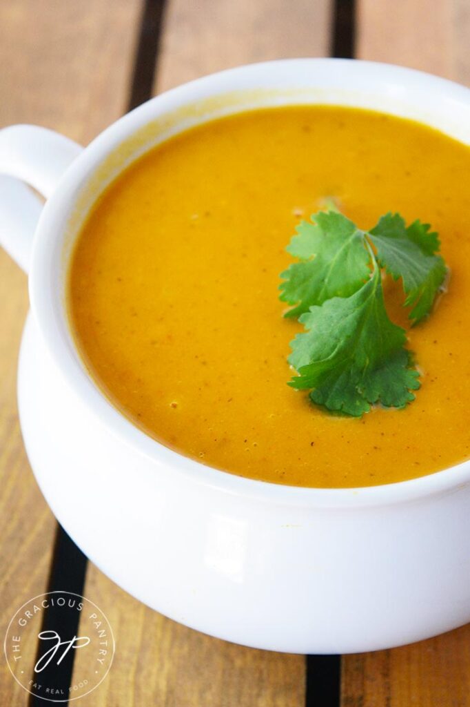 A white crock filled with Curried Sweet Potato Soup and garnished with fresh cilantro.