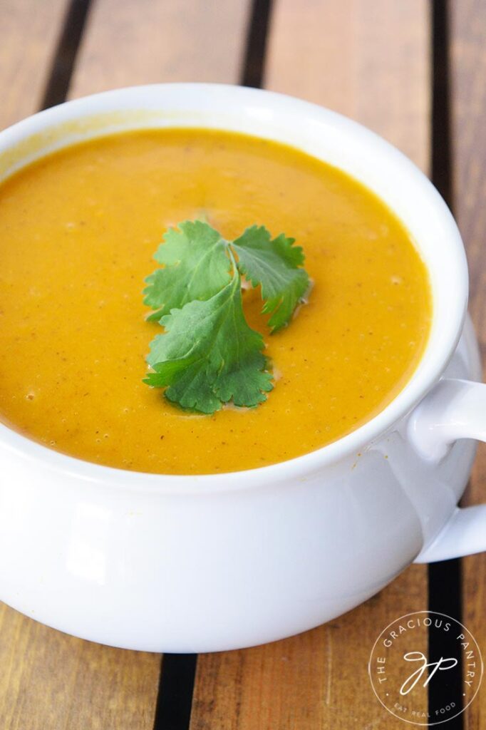 Curried sweet potato soup served in a white crock and garnished with fresh cilantro.