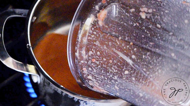 The blended strawberry sauce being poured into a pot.