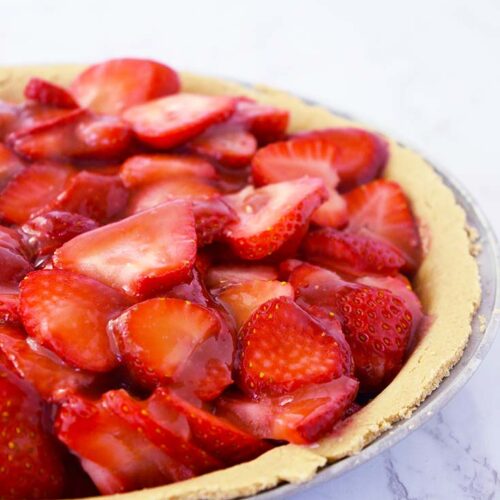 A side view of an uncut, fresh strawberry pie on a white background.