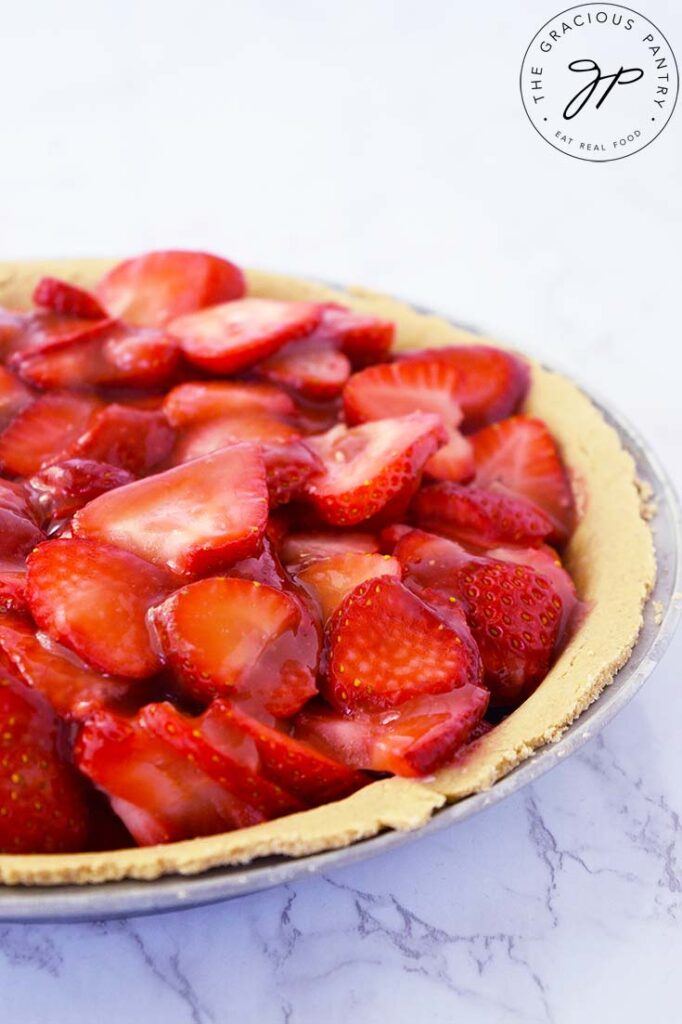 A side view of an uncut, fresh strawberry pie on a white background.