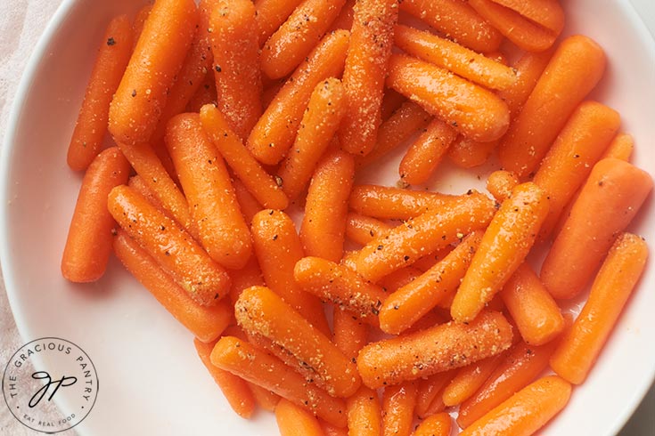 Raw baby carrots in a white bowl, seasoned with oil and spices.