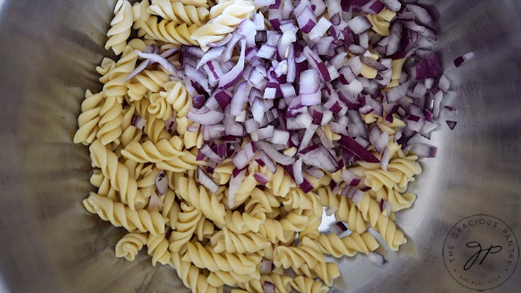 Chopped onions added to cooked pasta in a stainless steel mixing bowl.