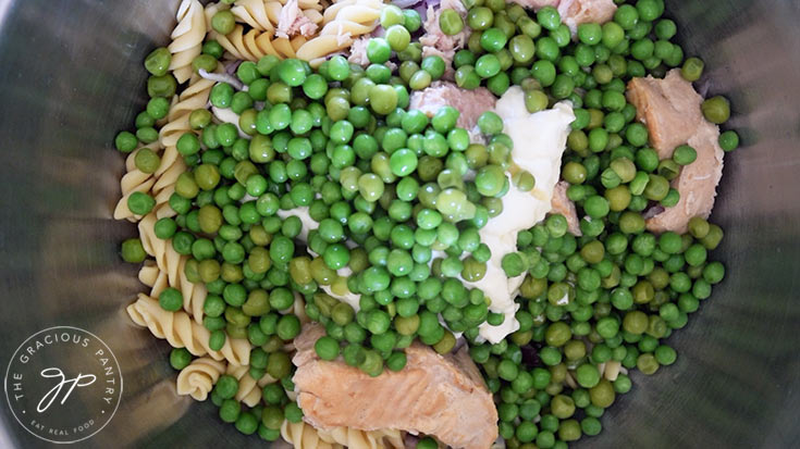 Cooked peas added to mayo, tuna, onions and cooked pasta in a mixing bowl.