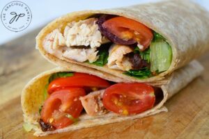 A just-made, Italian Chicken Wrap, sliced in half and stacked on a wooden surface.