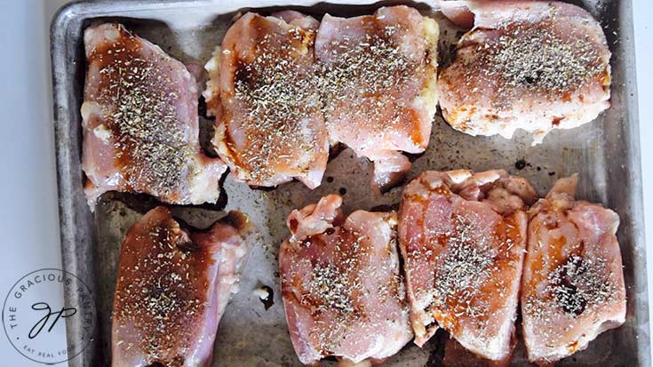 Raw chicken thighs, seasoned and sitting on a baking pan.