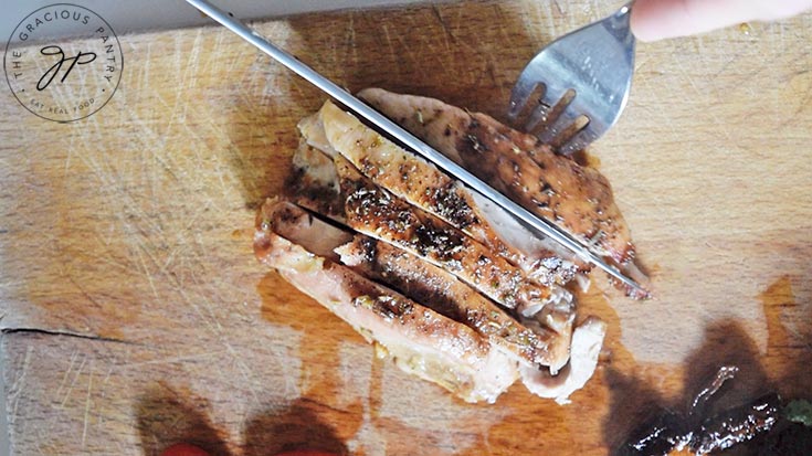 A chicken thigh being sliced on a wooden cutting board.