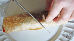 A rolled up wrap being cut in half on a white plate.