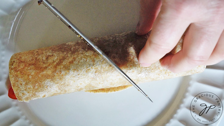 A rolled up Italian chicken wrap being cut in half on a white plate.