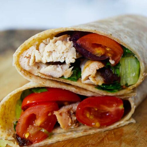 A front view of an italian chicken wrap, cut in half and stacked on a wooden surface.