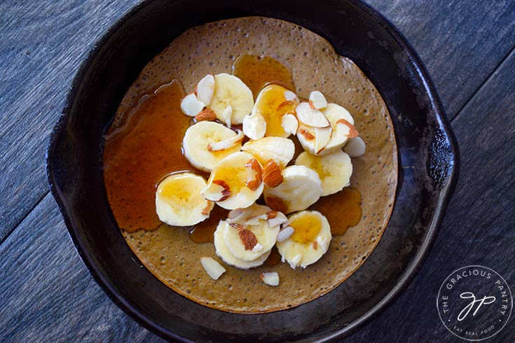 The finished skillet pancake topped with sliced bananas, sliced almonds and maple syrup.