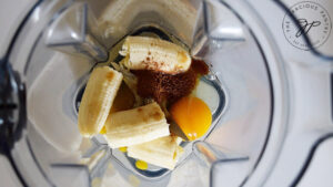 Eggs, a banana, cinnamon and vanilla extract sitting in a blender cup.