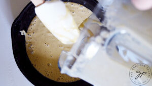 Skillet pancake batter being poured into an oiled skillet.