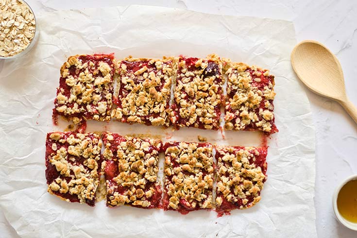 Cut healthy strawberry crumb bars sitting on a piece of white parchment paper.