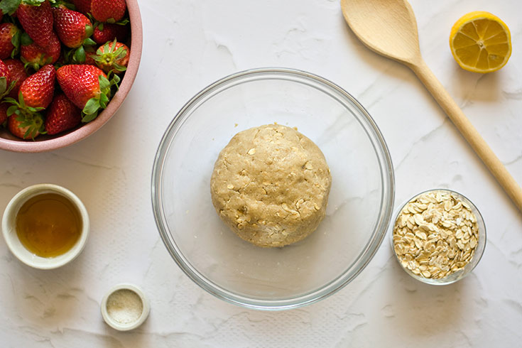 Dough for strawberry crumb bar crust sitting mixed in a glass mixing bowl.