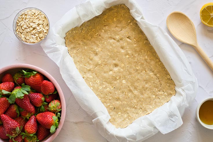 Healthy strawberry crumb bars crust pressed into a parchment-lined baking pan.