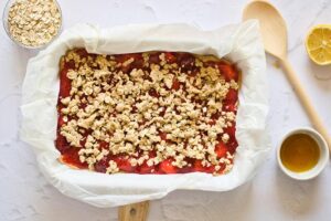Dough crumbs sprinkled over the top of strawberry sauce and crust in a baking pan.