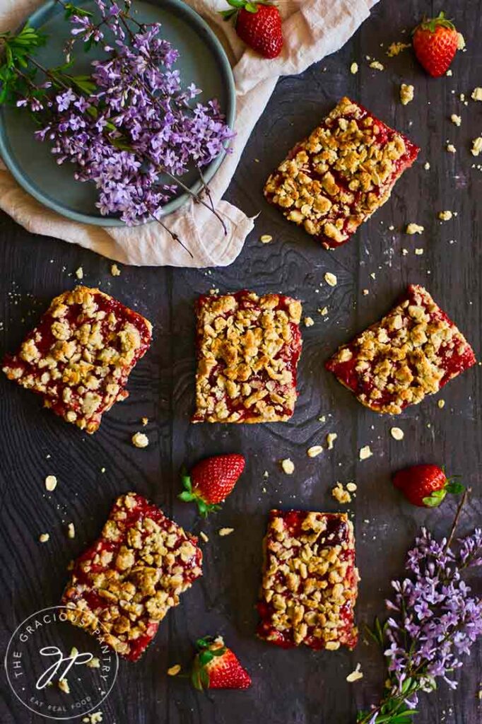 An overhead shot of healthy strawberry crumb bars laid out on a dark gray surface.