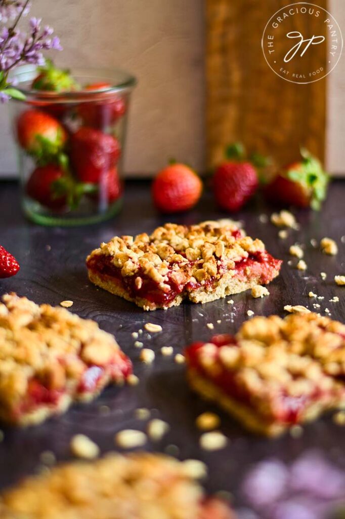 Healthy strawberry crumb bars laid out on a gray surface with a glass jar of fresh berries sitting behind them.