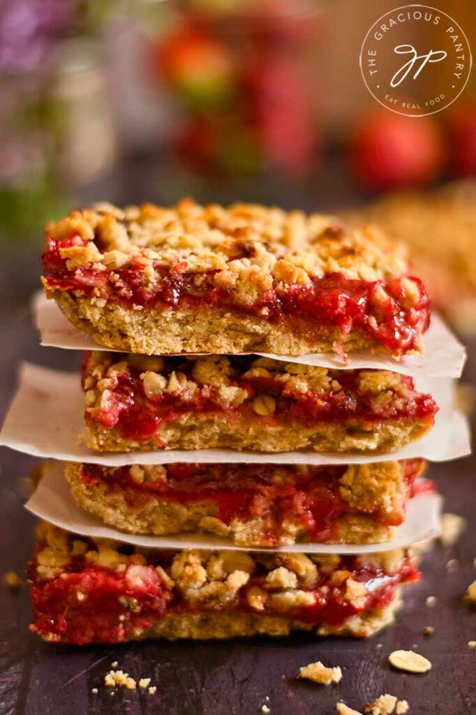 A stack of healthy strawberry crumb bars sit on a dark surface with pieces of parchment between each bar.