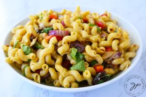 A bowl of Tuscan pasta salad in a white bowl sitting on a white marble surface.