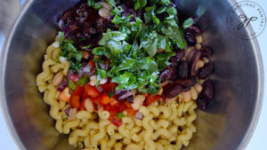 Fresh basil leaves added to a mixing bowl of pasta and chopped veggies.