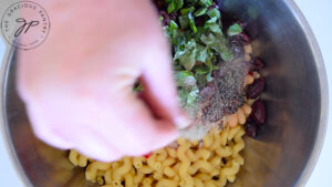 Seasoning the Tuscan pasta salad with pepper and salt.