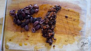 Chopped Kalamata olives and sun-dried tomatoes sitting on a cutting board.