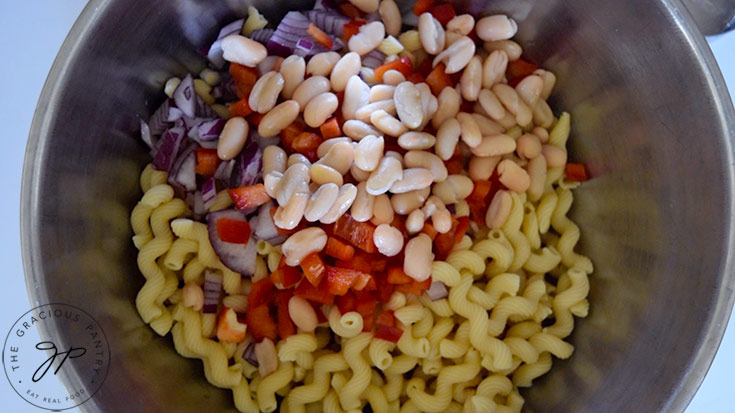 Cannellini beans added to the peppers, onions and cooked pasta in a mixing bowl.