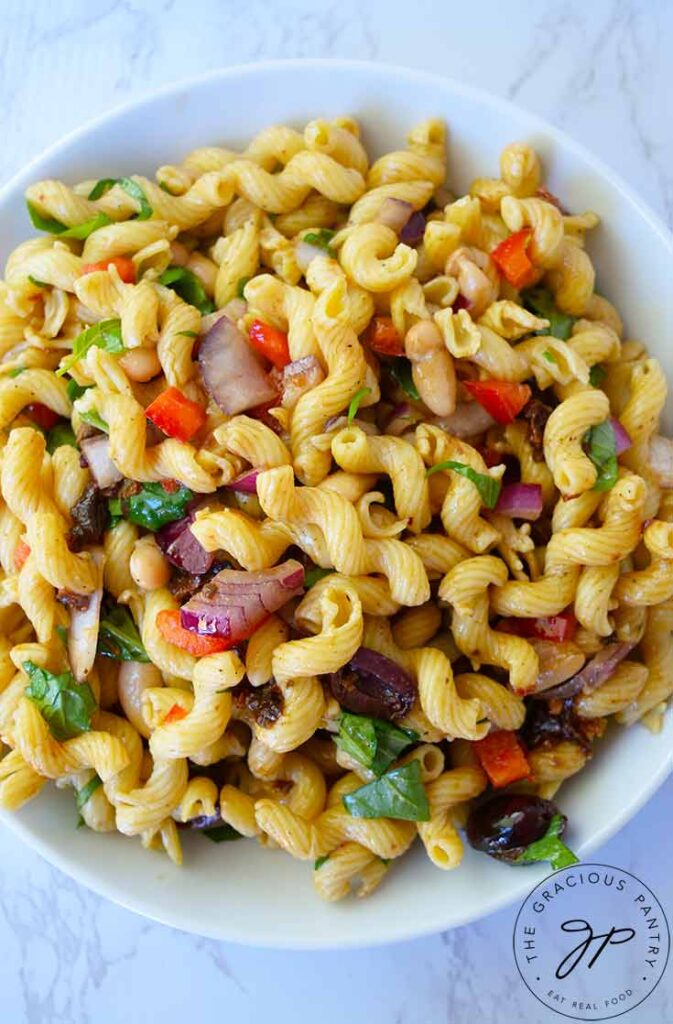 An overhead view of a white bowl filled with Tuscan pasta salad.