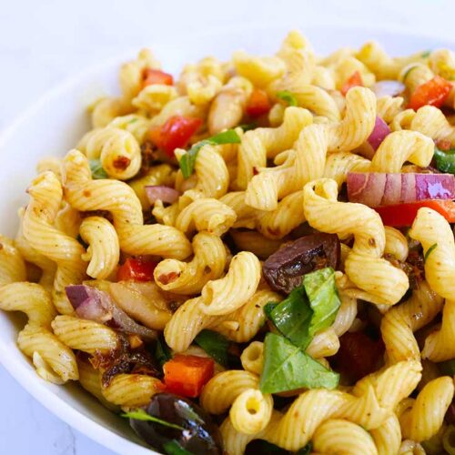 A front view of a white bowl filled with Tuscan pasta salad.