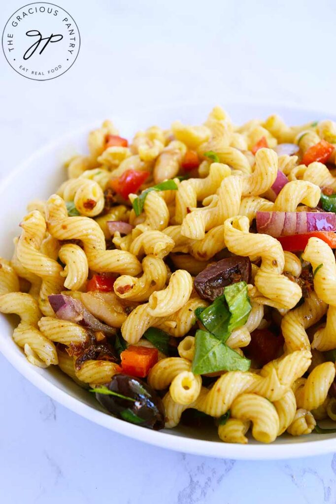 A front view of a white bowl filled with Tuscan pasta salad.