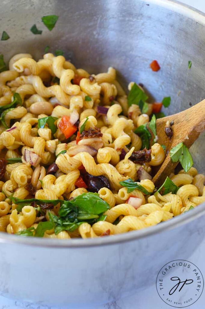 Just mixed Tuscan pasta salad sitting in a stainless steel mixing bowl.