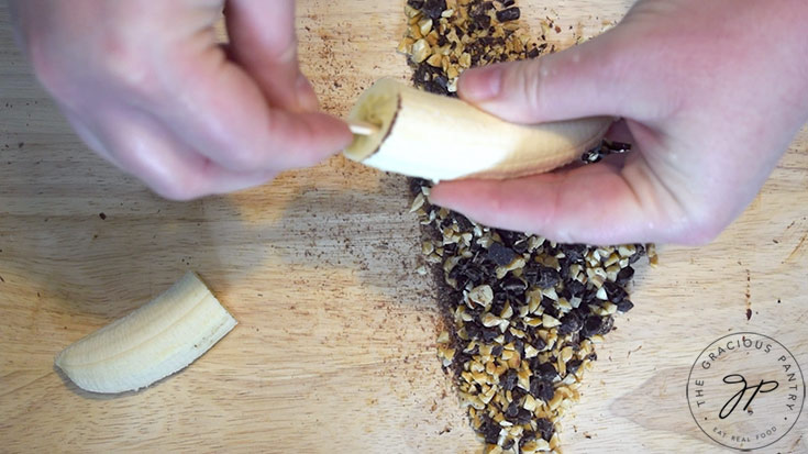 Hands inserting a popsicle stick into one end of a half a banana.