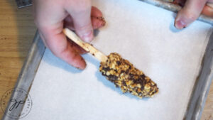 A hand placing a banana popsicle on a parchment-lined cookie sheet.
