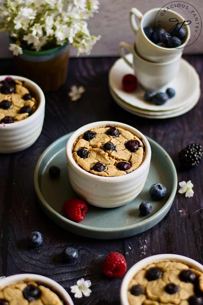 Several ramekins of blended baked oatmeal sitting on a table surrounded by fresh berries, flowers and some tea cups.