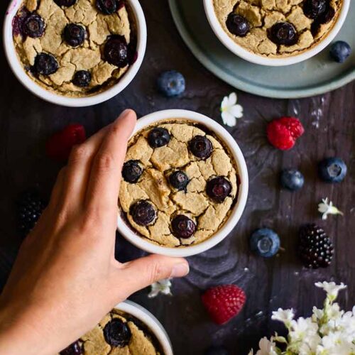 A female hand reaches for a ramekin of Blended Baked Oatmeal.