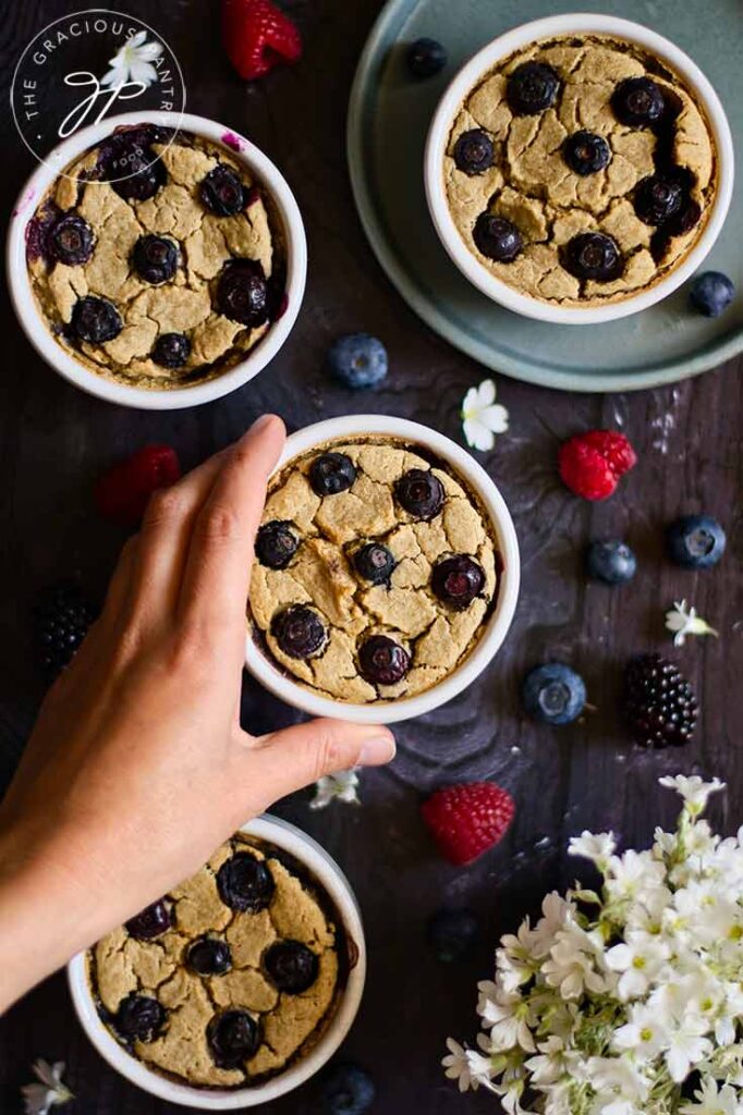 A female hand reaches for a ramekin of Blended Baked Oatmeal.