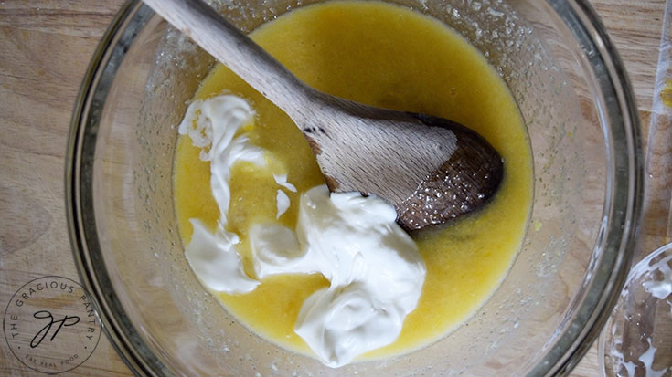 Yogurt added to blueberry cake batter in a mixing bowl.