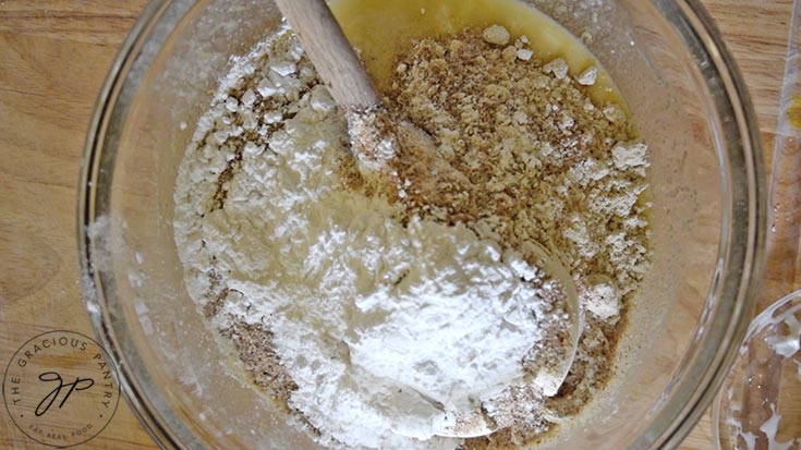 Flour and psyllium husks added to blueberry cake batter in a glass mixing bowl.