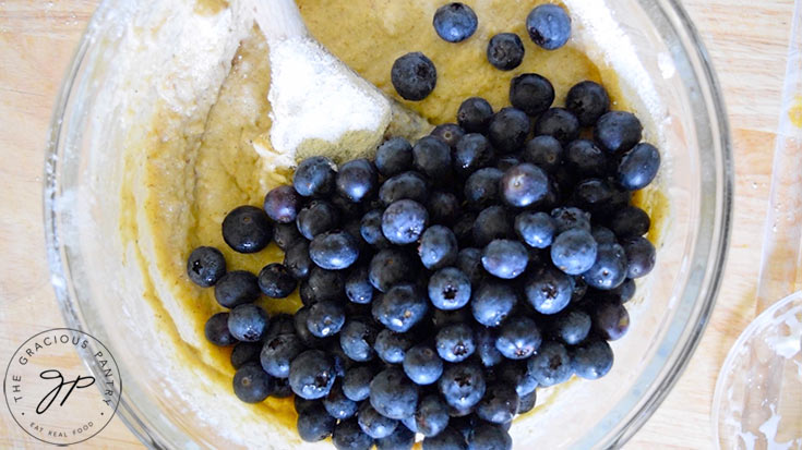 Fresh blueberries added to blueberry cake batter in a glass mixing bowl.
