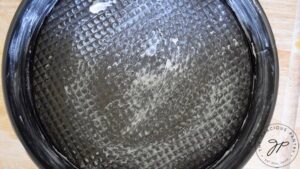 A round cake pan that has been greased with butter.