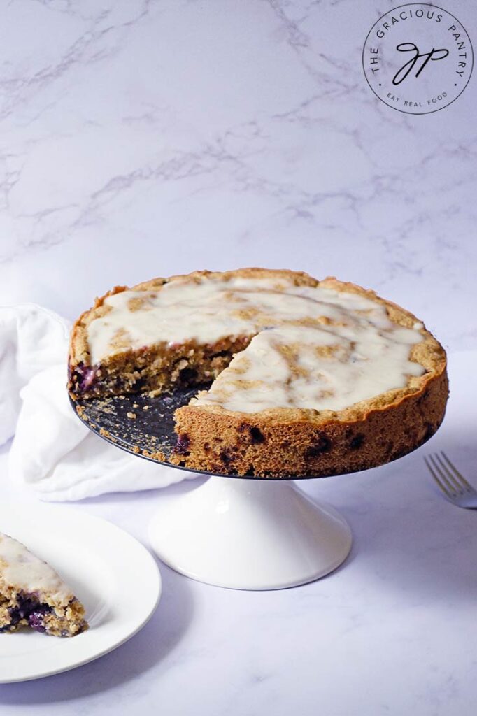 A side angle shot of a blueberry cake on a cake stand with one slice removed.