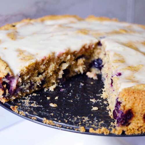 A close up shot of a blueberry cake with a slice removed.