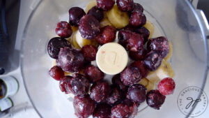 Frozen cherries and banana slices sitting in a food processor before blending.