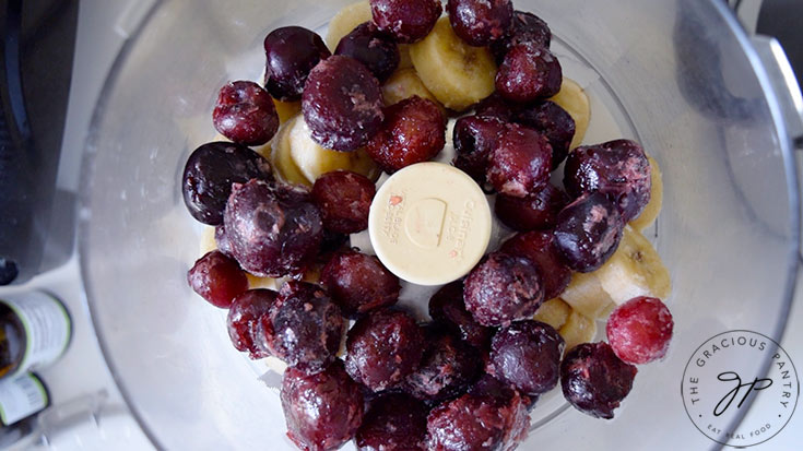 Frozen cherries and banana slices sitting in a food processor before blending.
