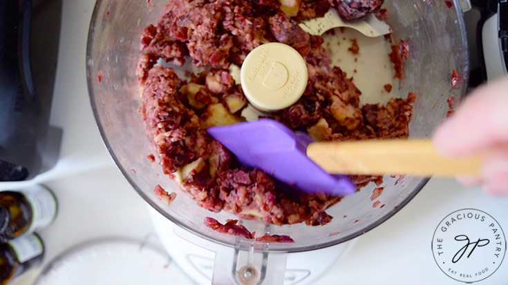 Scraping the sides of the food processor halfway through blending.