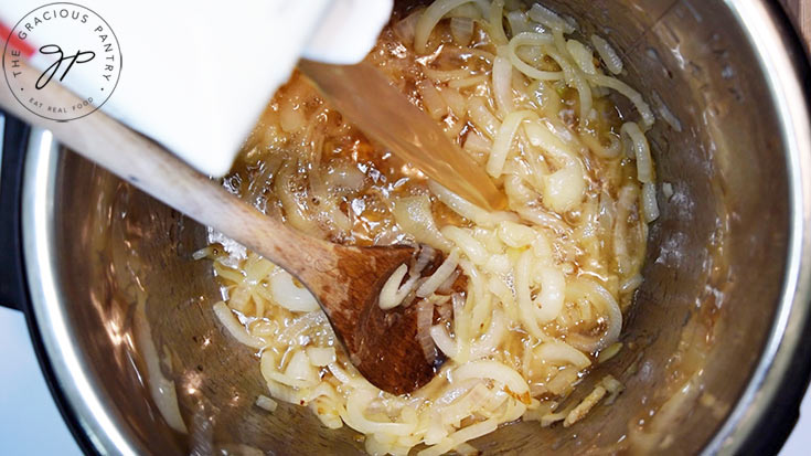 Broth is being poured into sautéd onions in an instant pot.