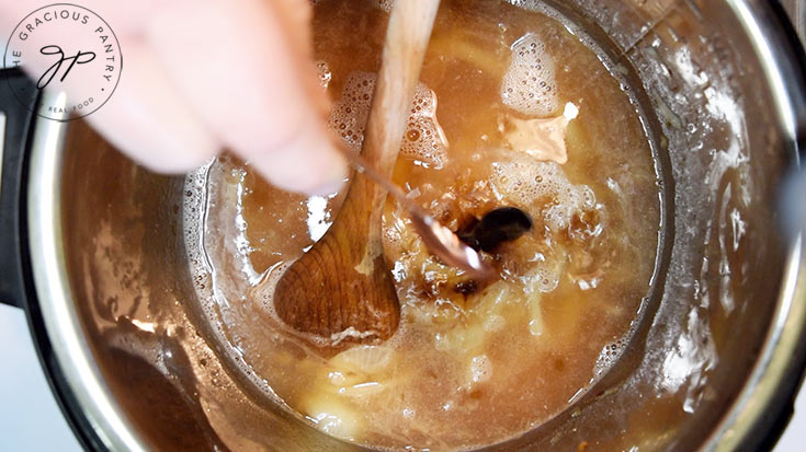 Balsamic vinegar being stirred into broth and onions in an Instant Pot.