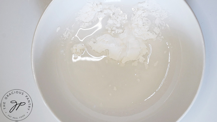 A white bowl with water and arrowroot powder in it. This makes a slurry for thickening the french onion chicken sauce.